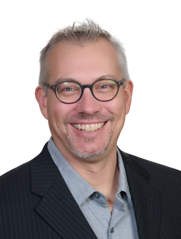 A middle-aged man wearing glasses, a gray shirt, and a dark pinstripe blazer smiles at the camera against a plain white background.